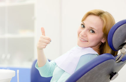 A woman giving a thumbs up in a dental chair