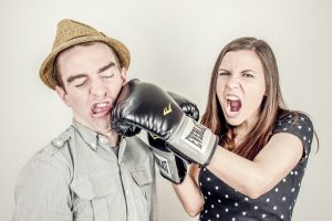 A woman with a boxing glove punching a man in a hat. 